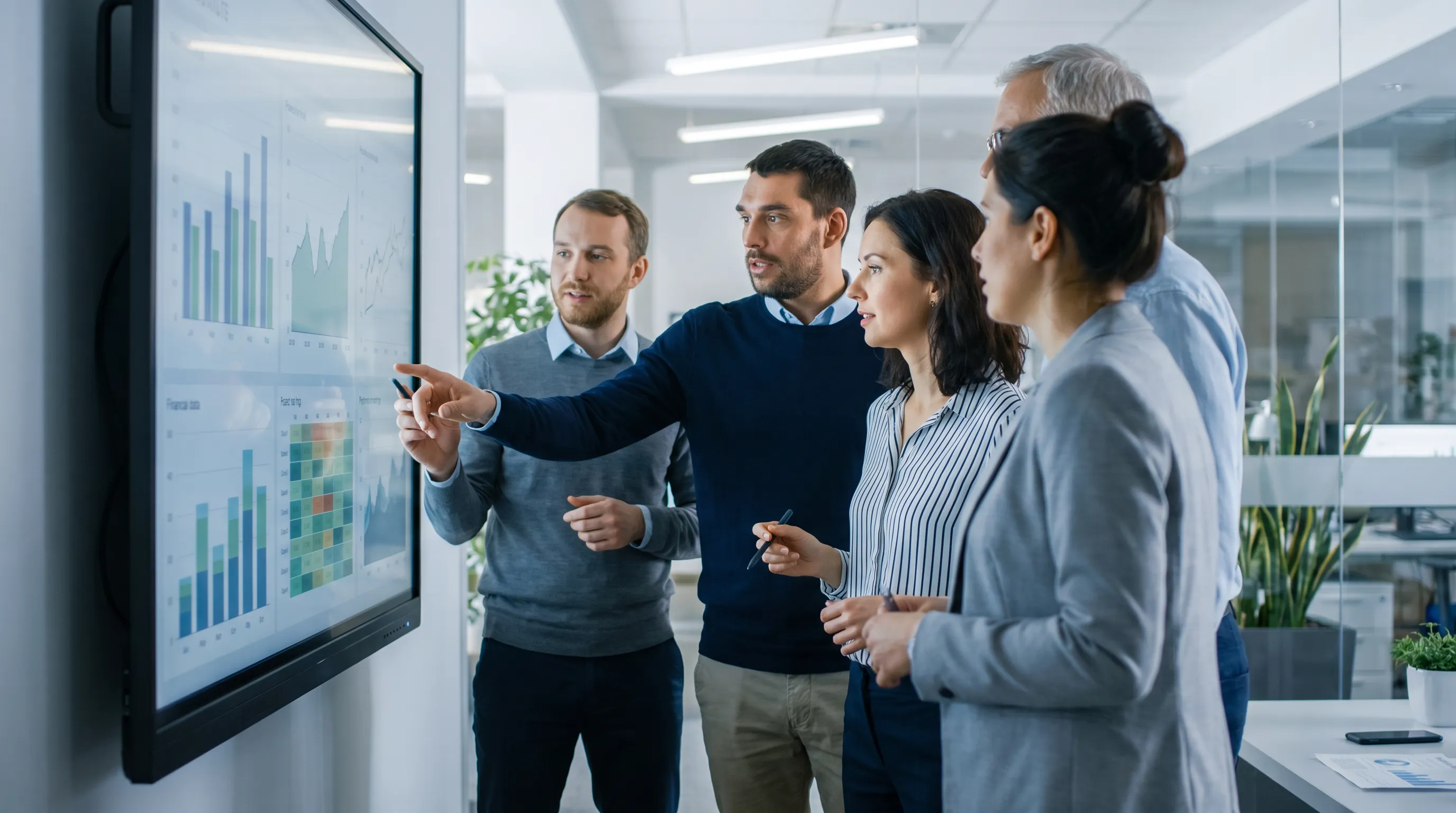 A group of business consultants collaborates in a modern office, focused on a digital screen displaying financial data and graphs.