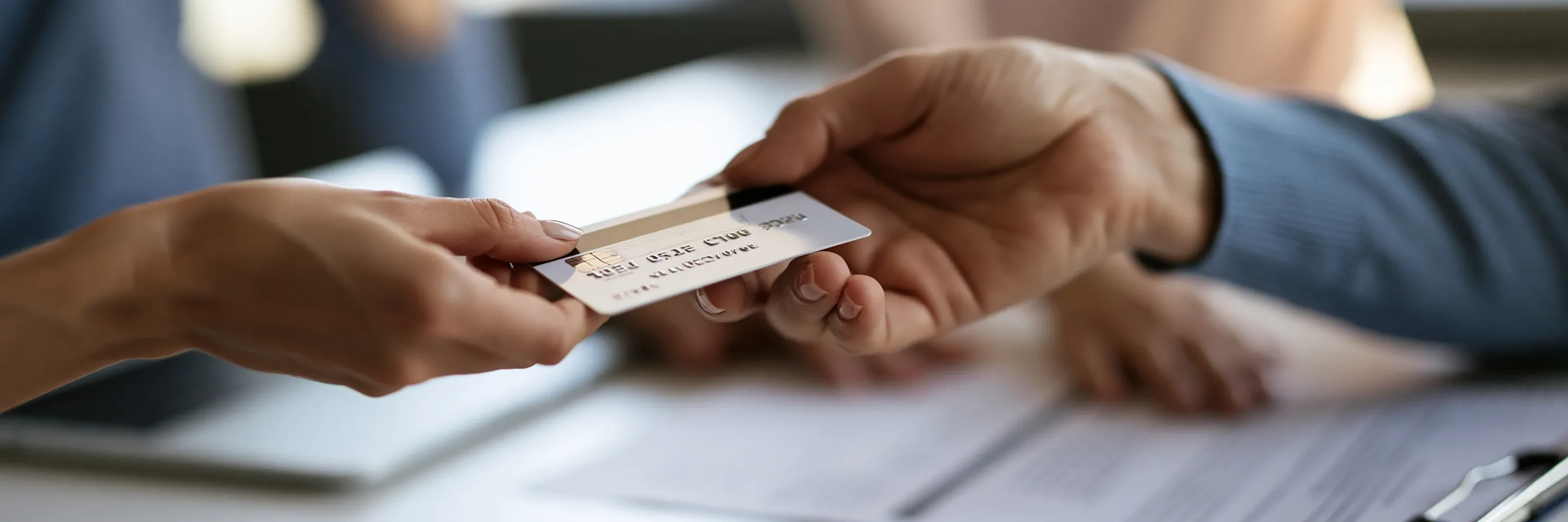 Close-up of a customer handing a credit card to a business representative, illustrating payment processing, financial transactions, customer verification, banking services, and secure commerce.